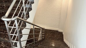 Una escalera con barandilla de metal, escalones de mármol negro y pared con textura.