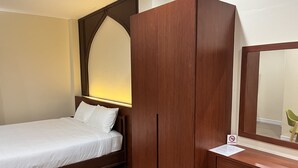 Un dormitorio con una cama, un armario de madera, un escritorio con silla y un espejo.
