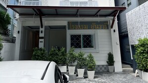 Exterior del Hotel Anwari, con fachada blanca, adornos de celosía y un letrero en inglés y tailandés.