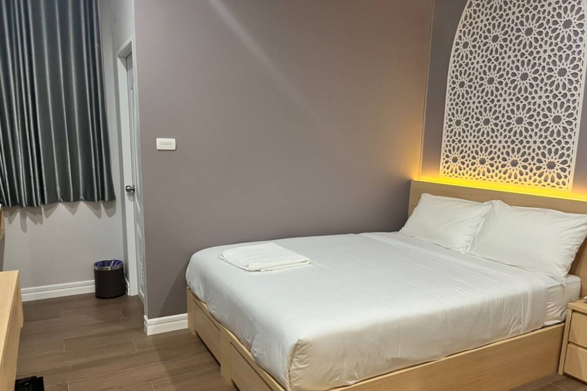 A neatly made bed with white linens, a wooden headboard, and a decorative wall panel.