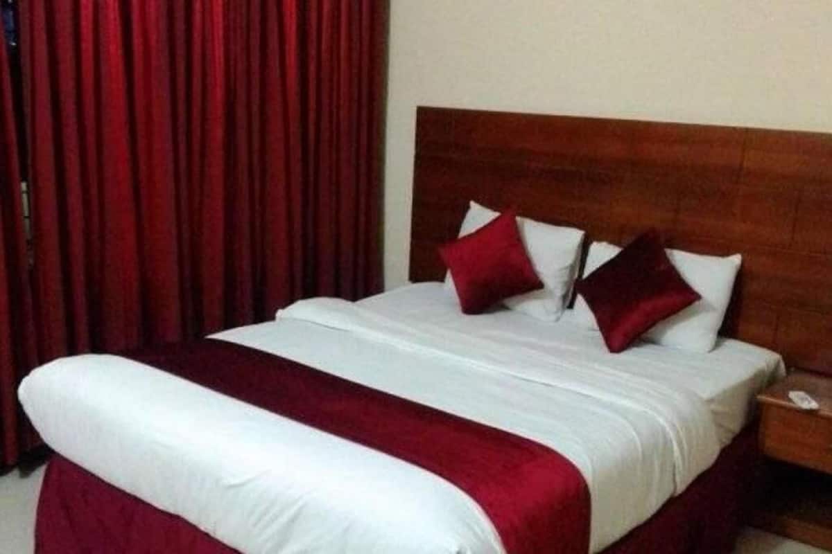 A hotel room with a bed, red curtains, a wooden headboard, and a nightstand.
