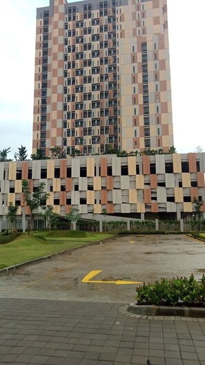 A modern high-rise building with a patterned facade and a parking area in front. - S&A Property 2 (Tarumajaya)