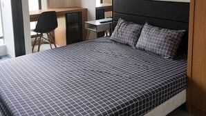 Ein Schlafzimmer mit Bett, Schreibtisch und Stuhl. Ein Fenster mit Vorhängen ist vorhanden.