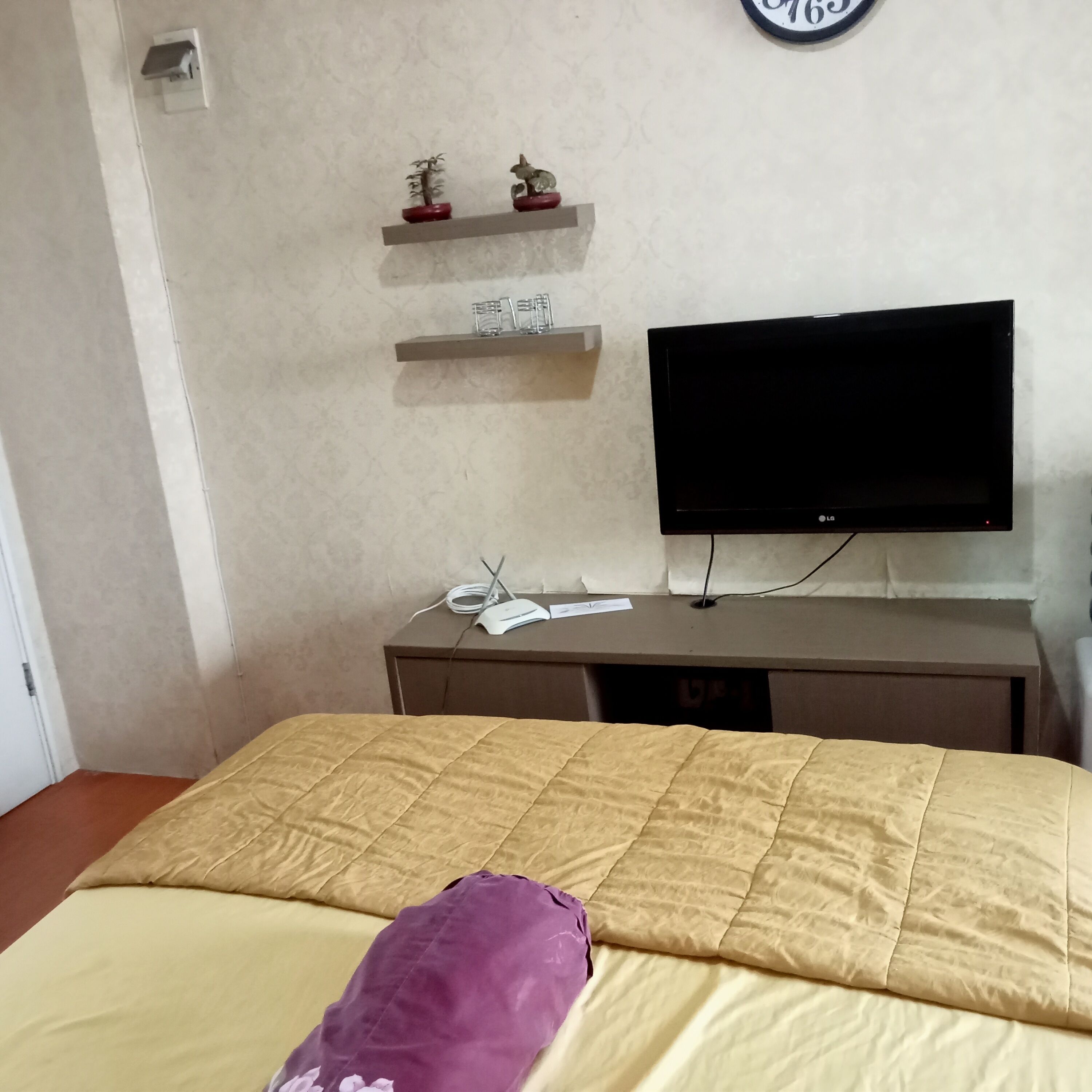 Une chambre à coucher comprenant un lit, une télévision, un bureau et deux étagères ornées d’objets décoratifs.