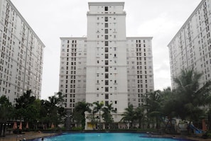 A high-rise residential building with a central courtyard featuring a swimming pool, surrounded by palm trees and lounge areas. - S&A Property 3 (Jakarta)