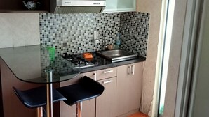 Une cuisine moderne avec une table à plateau en verre, deux tabourets de bar, un évier en acier inoxydable et un crédence carrelée.