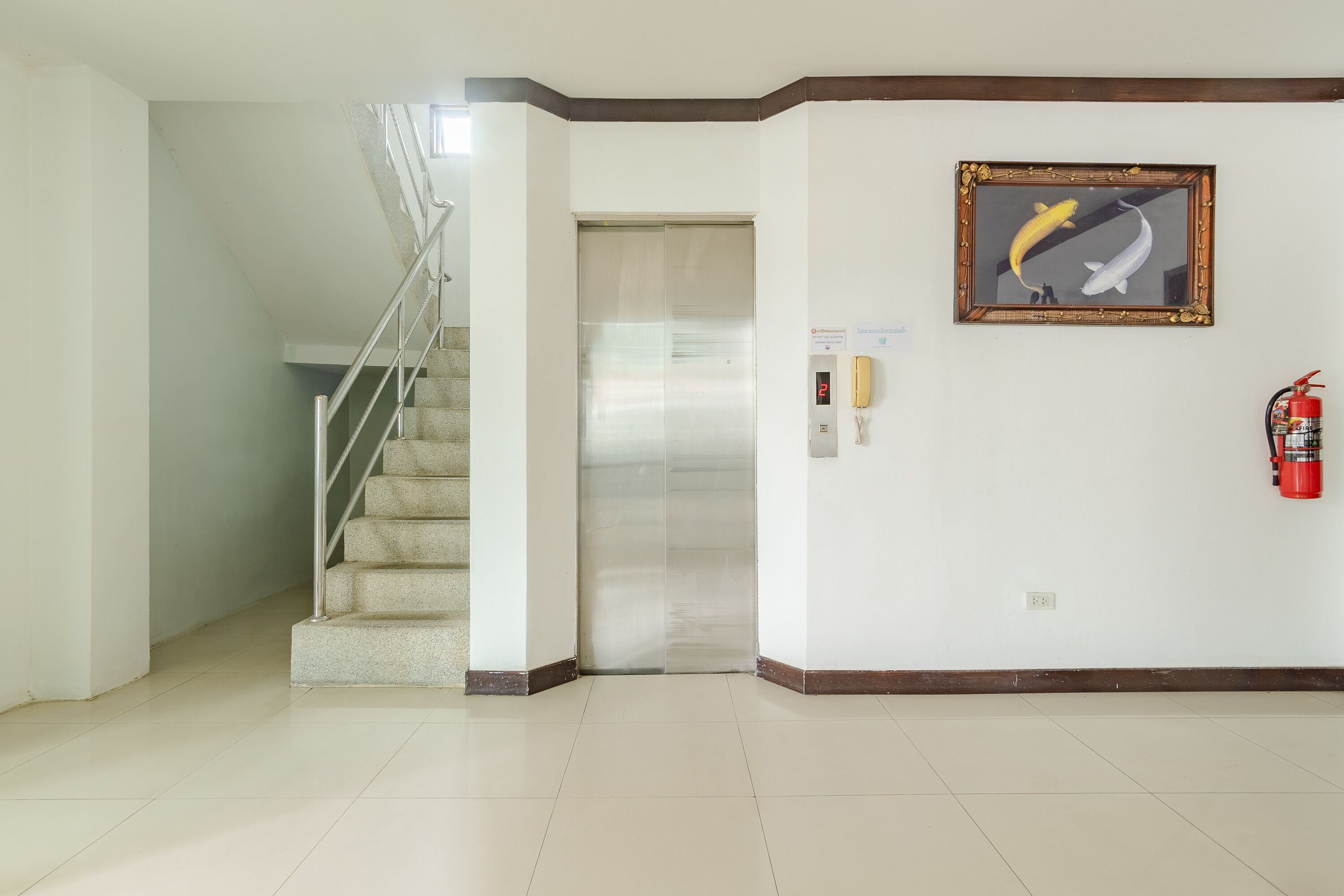 A clean, modern lobby with a staircase, an elevator, a framed picture of a fish, and a fire extinguisher on the wall.