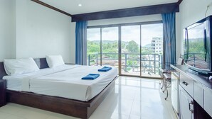 A hotel room with a large bed, a TV, and a balcony with a view of buildings and greenery. - Goodday Kathu (Kathu)