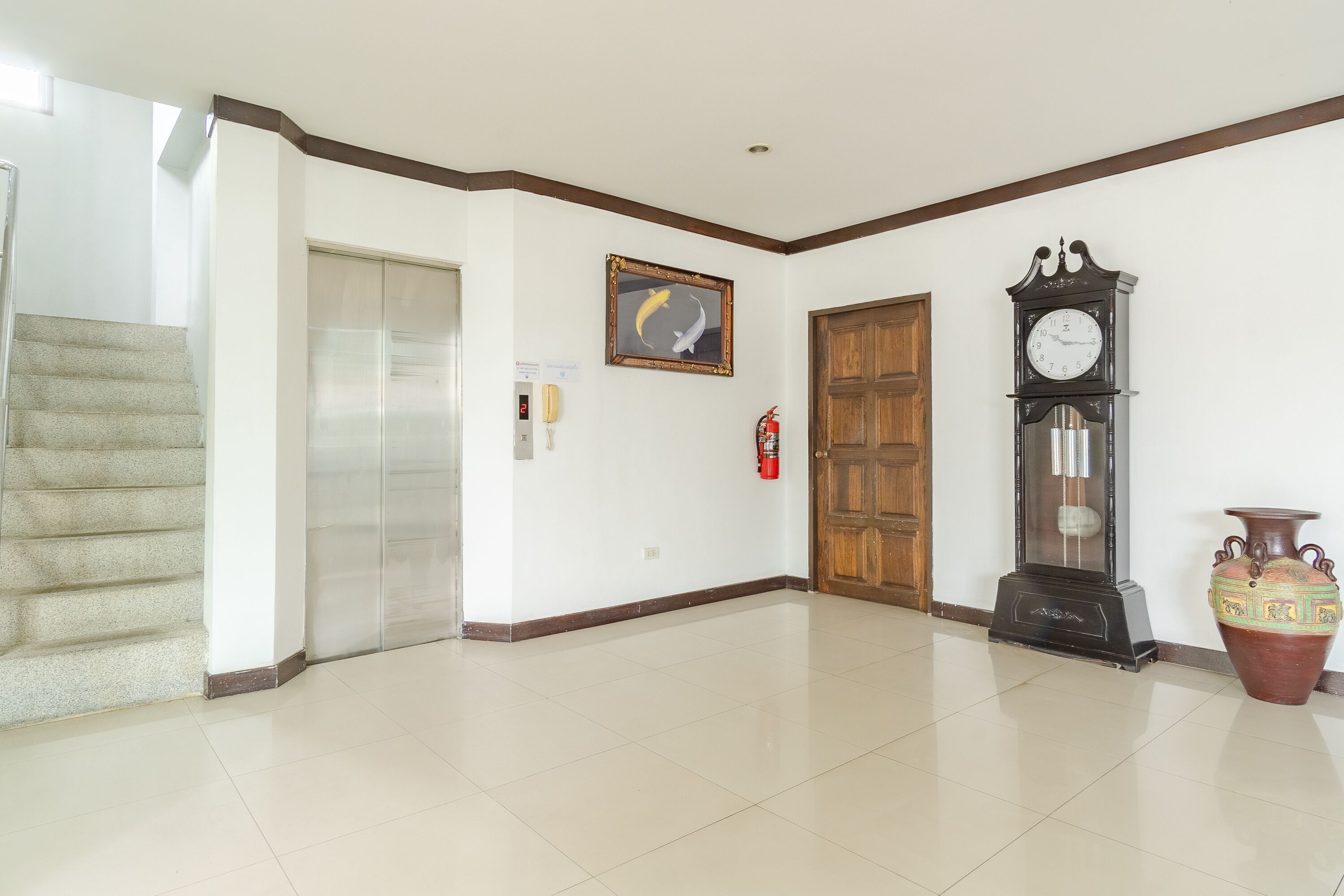 Un corridoio con una scala, una porta in legno, un orologio appeso al muro, un quadro incorniciato e un vaso.