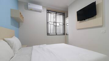 Habitación de hotel con cama, televisor montado en la pared, ventana con rejas y aire acondicionado.