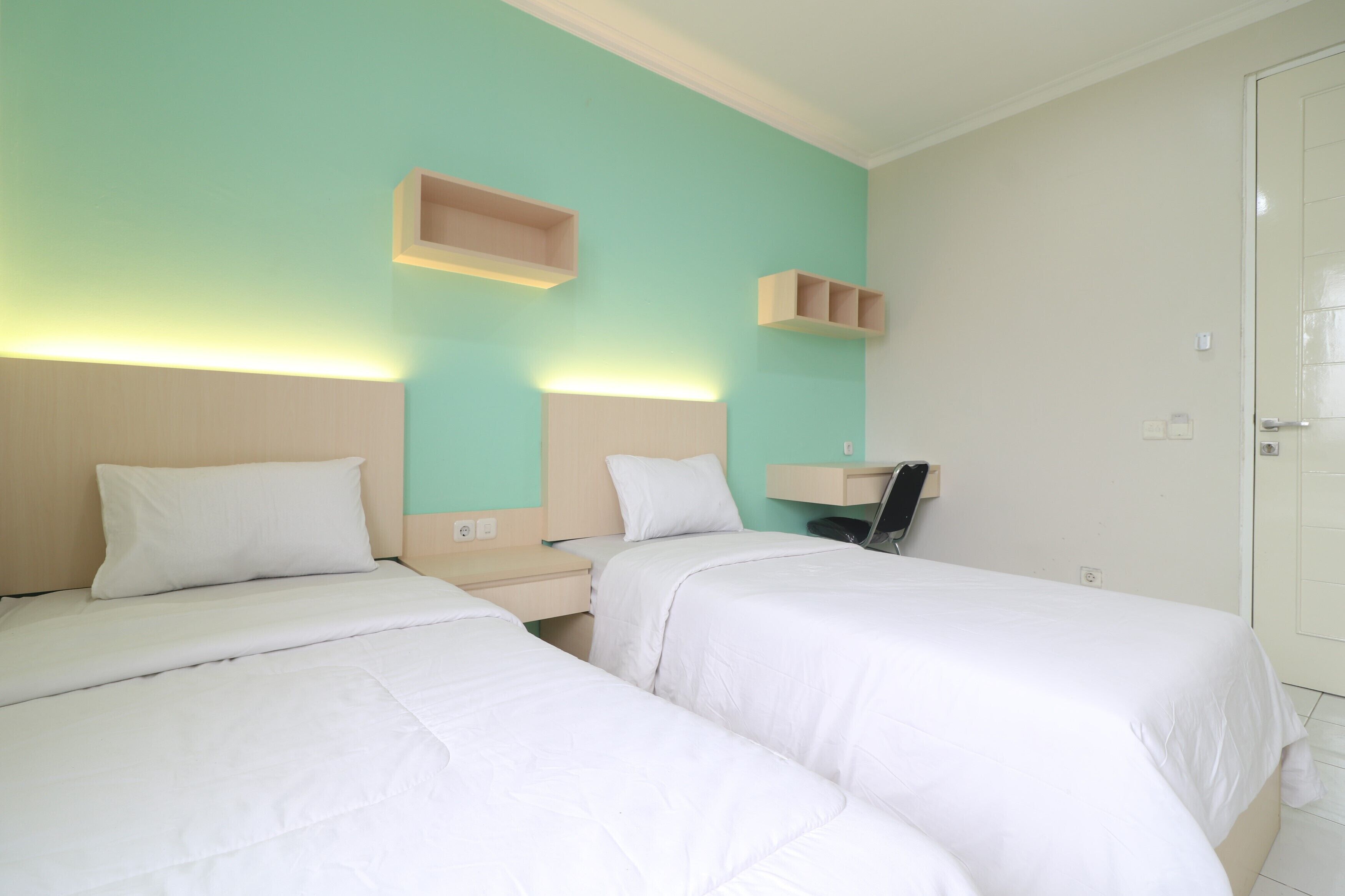 Una habitación de hotel con dos camas, una mesita de noche, un estante y una puerta.