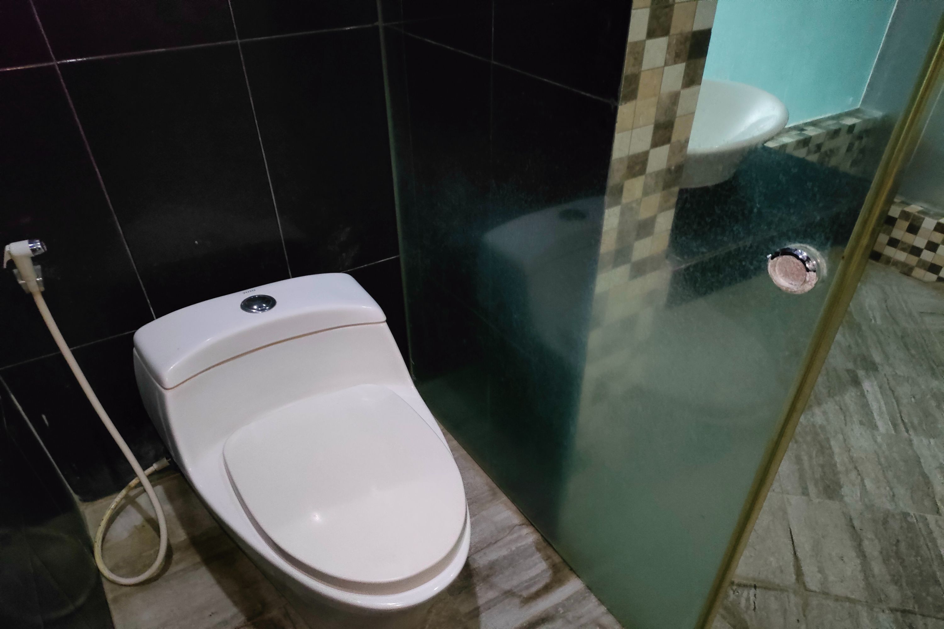 Un inodoro blanco con bidé, una cabina de ducha de vidrio y piso de cerámica.