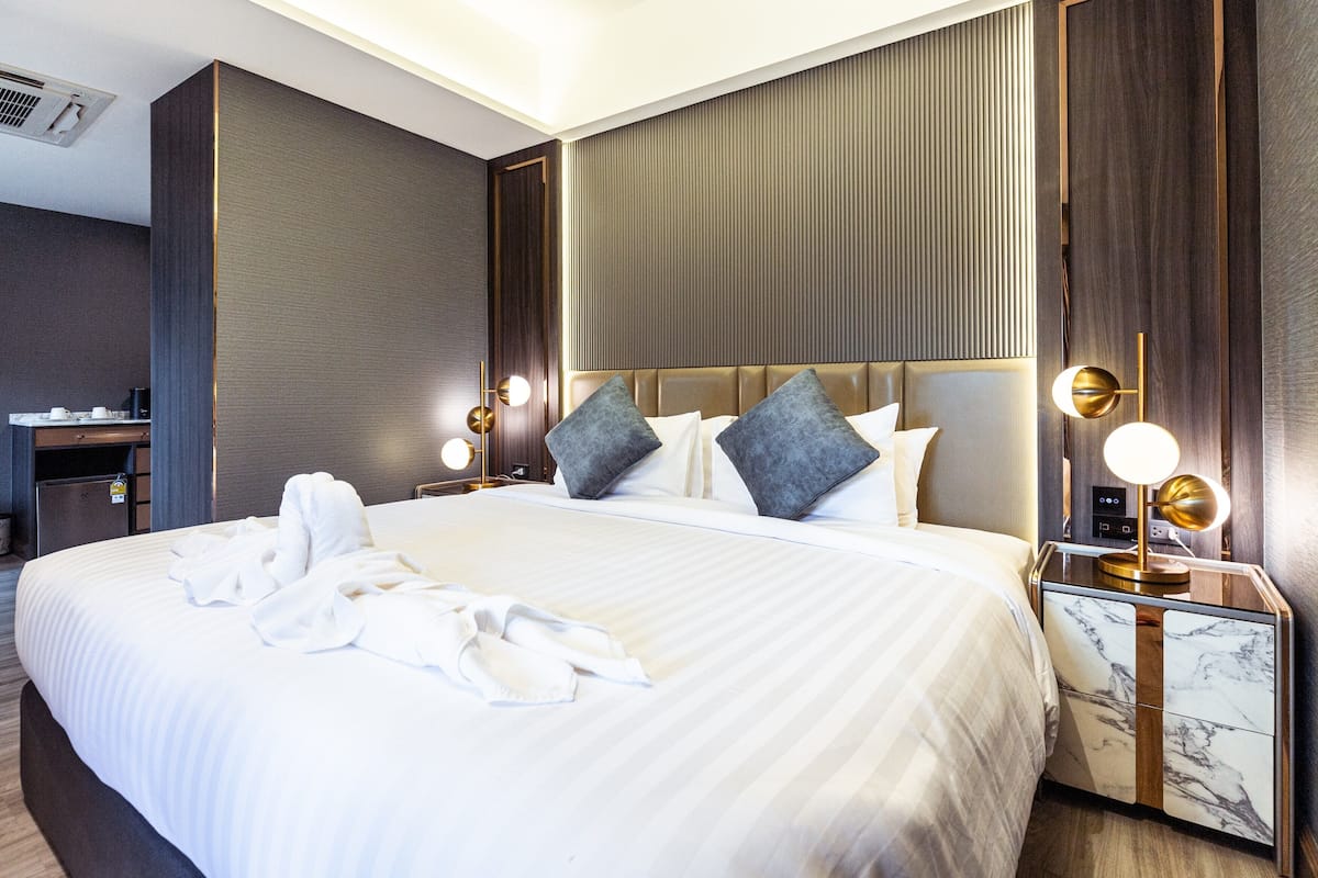 A hotel room with a large bed, a bedside table with a lamp, a wardrobe, and a desk with a chair.