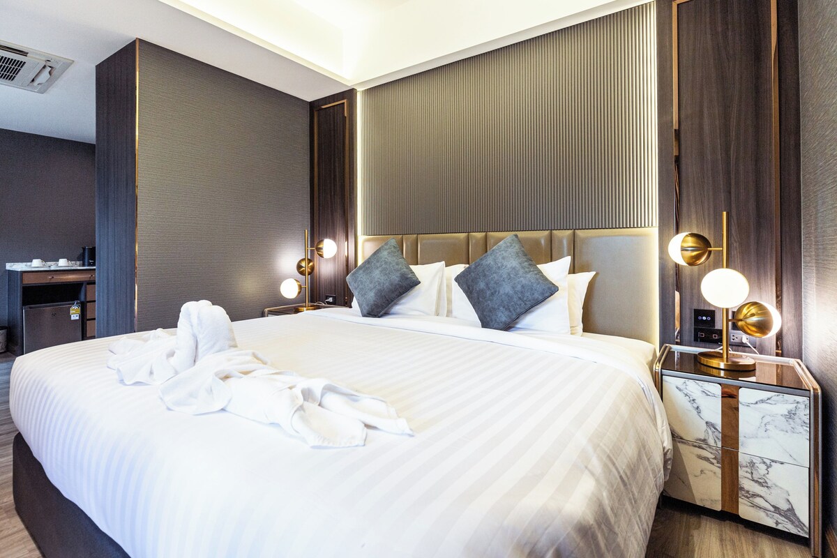 A hotel room with a large bed, two bedside lamps, a nightstand, and a minibar.