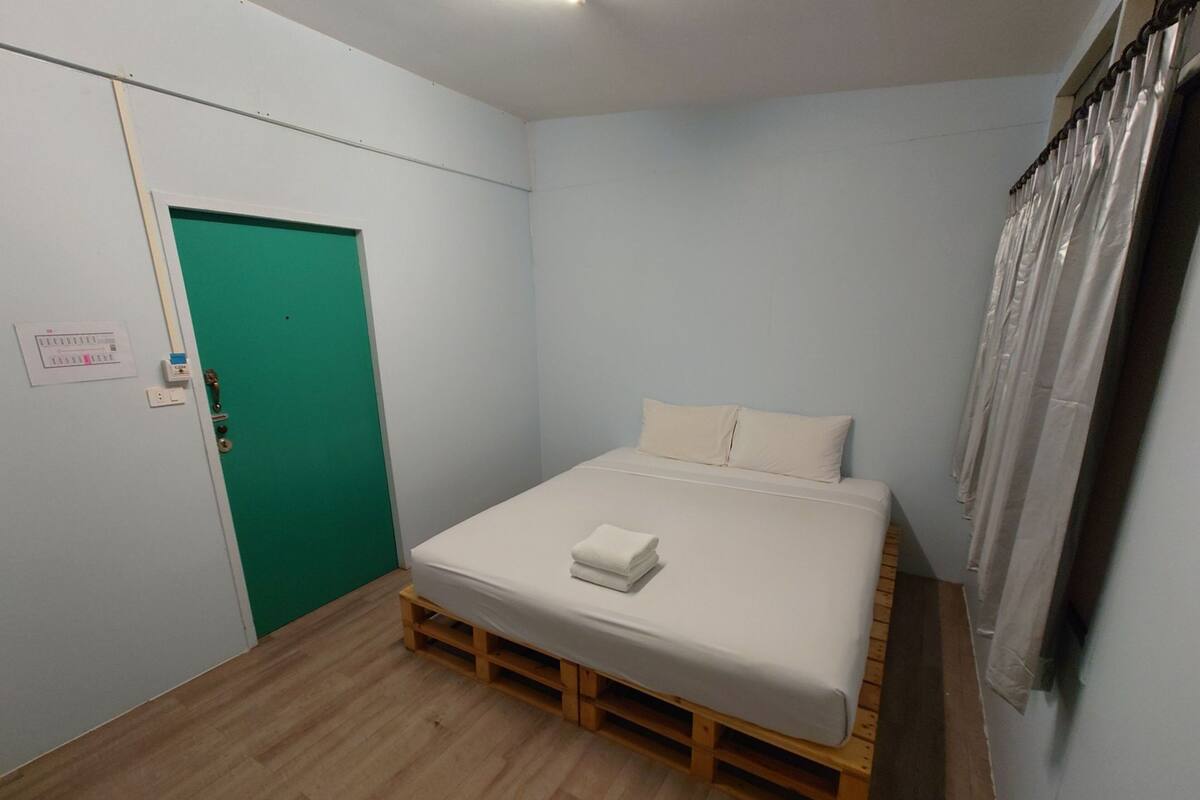 A bedroom with a bed on a wooden pallet, a green door, and a white wall.