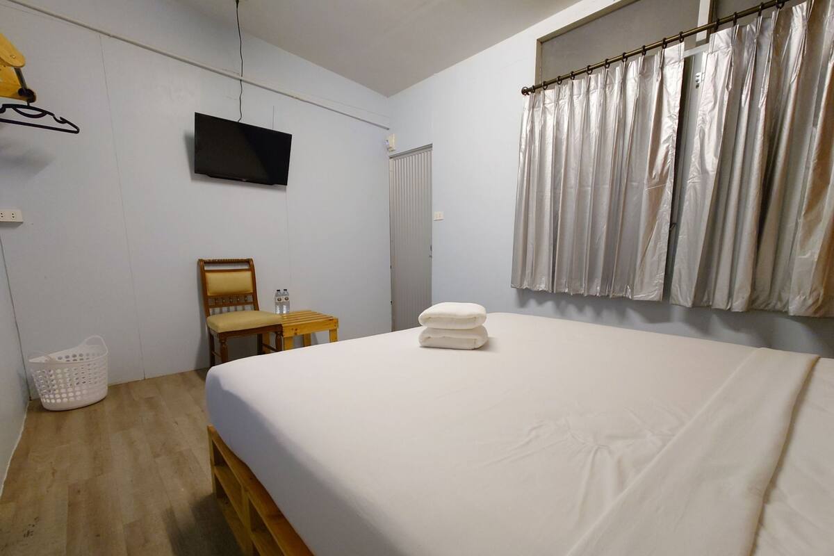A bedroom with a bed, a wooden chair, a small table, a TV, and a curtain.