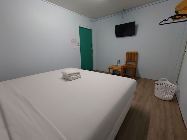 A hotel room with a bed, a chair, a television, and a door. - Baan Kim Lian Sha (Ratsada)