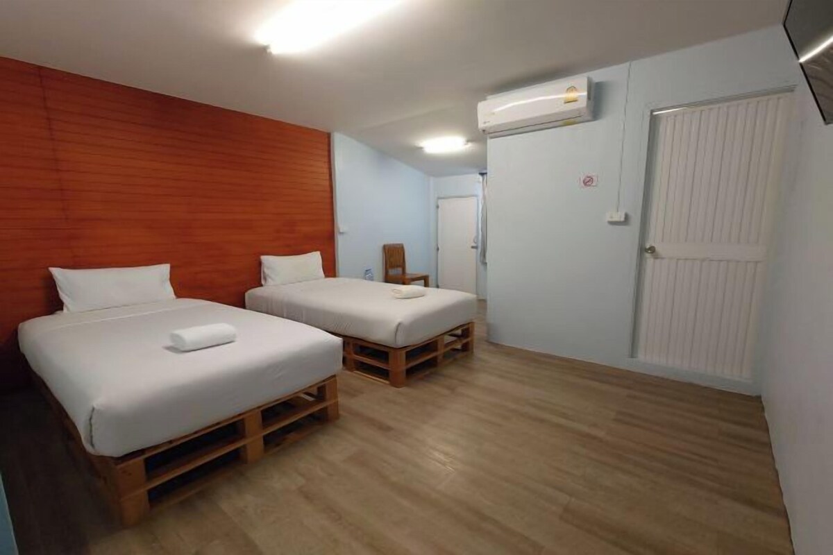 A room with two beds, wooden flooring, a white door, and an air conditioning unit.