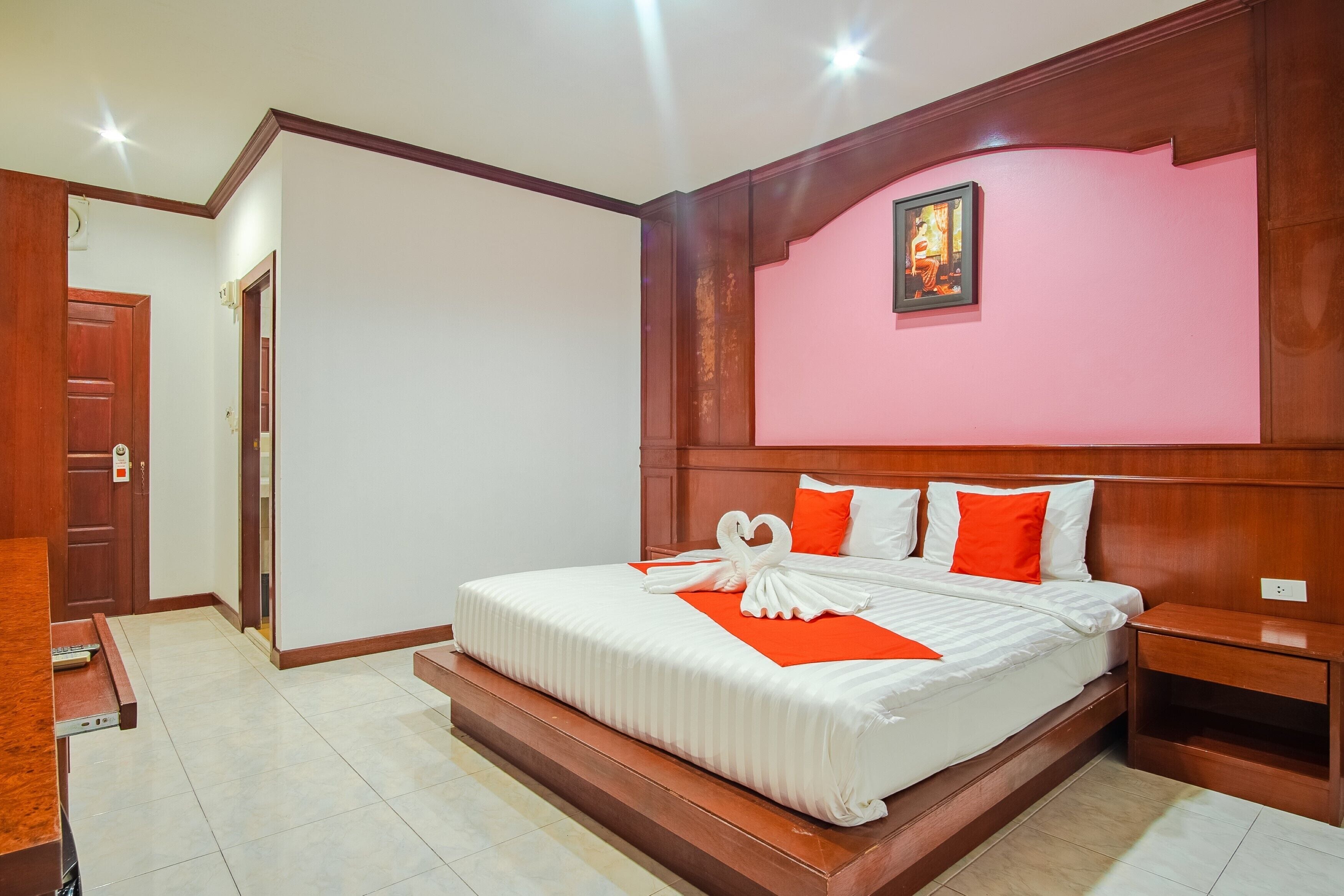 A hotel room with a large bed, wooden headboard, and a red accent wall.