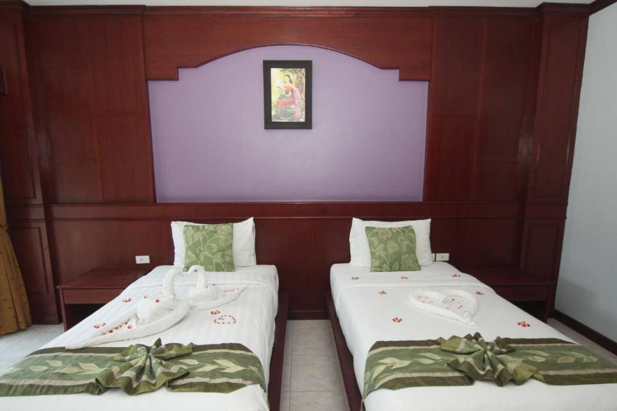 Een hotelkamer met twee bedden, elk met een witte spreidek, groene en witte kussens, en een decoratieve zwaan van handdoeken.