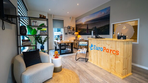 A modern living room with a sofa, a wooden reception desk labeled "EuroParcs," and a dining area with a table and chairs. - EuroParcs Texel (De Cocksdorp)