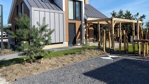 A modern house with a sloped roof, a wooden deck, and a gravel driveway. - EuroParcs Texel (De Cocksdorp)