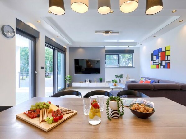 A modern living room with a dining area, a sofa, a TV, and a colorful abstract painting on the wall.