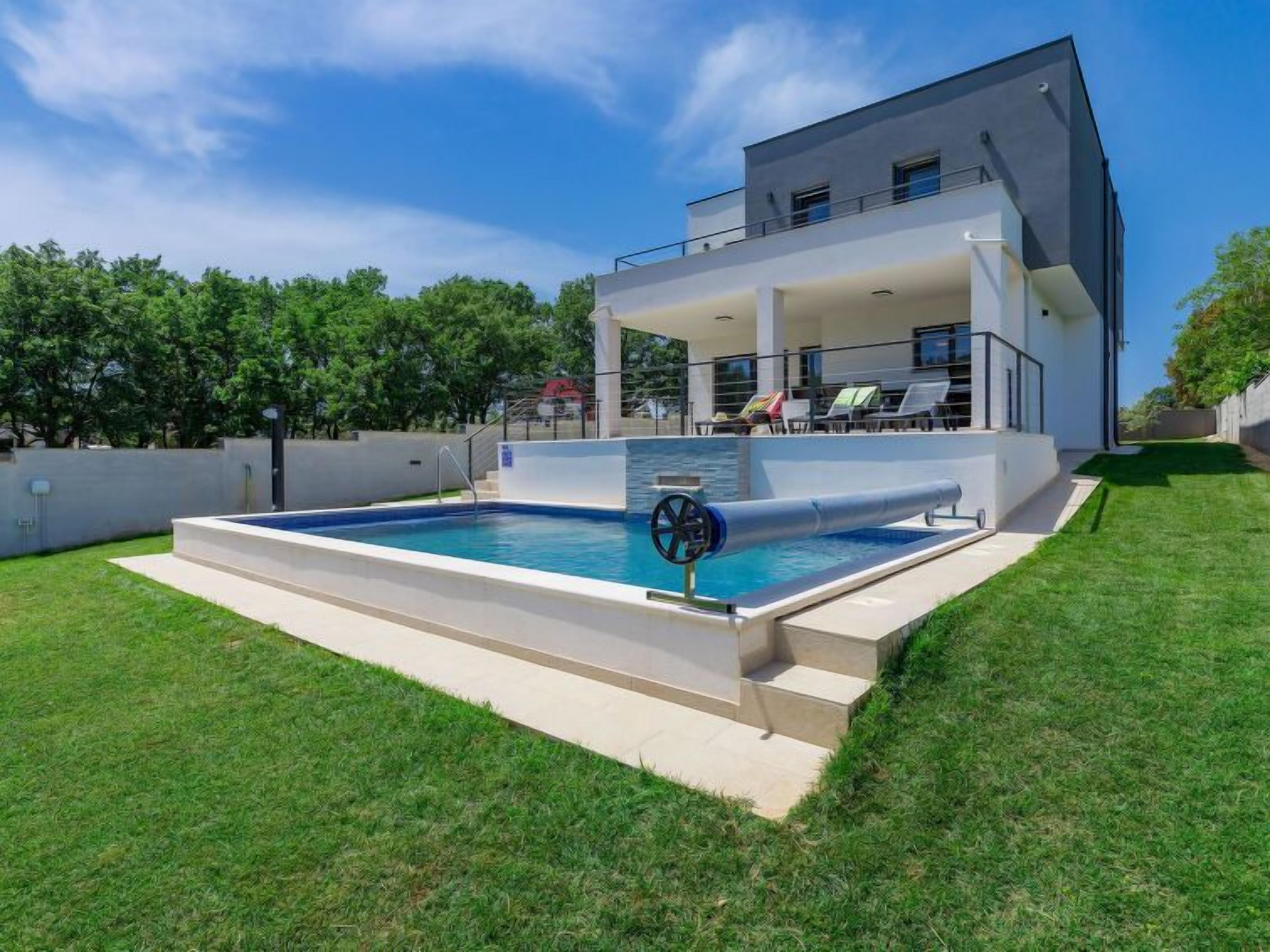 Ein modernes, zweistöckiges Haus mit Swimmingpool, überdachter Terrasse und gepflegtem Rasen.