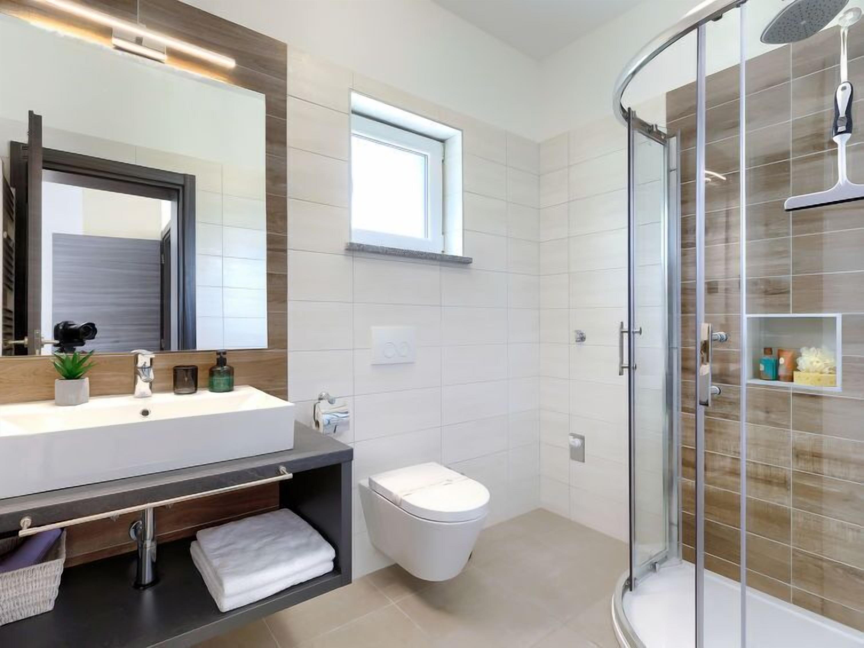 A modern bathroom with a large mirror, a sink, a toilet, and a glass-enclosed shower.