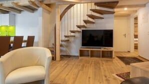 Een moderne woonkamer met een houten trap, een flatscreen televisie en een eethoek met een tafel in groen licht.