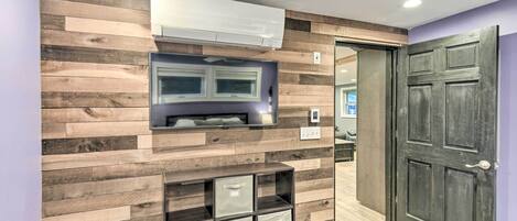 A modern room with a wooden wall panel, built-in storage, a flat-screen TV, and a door.