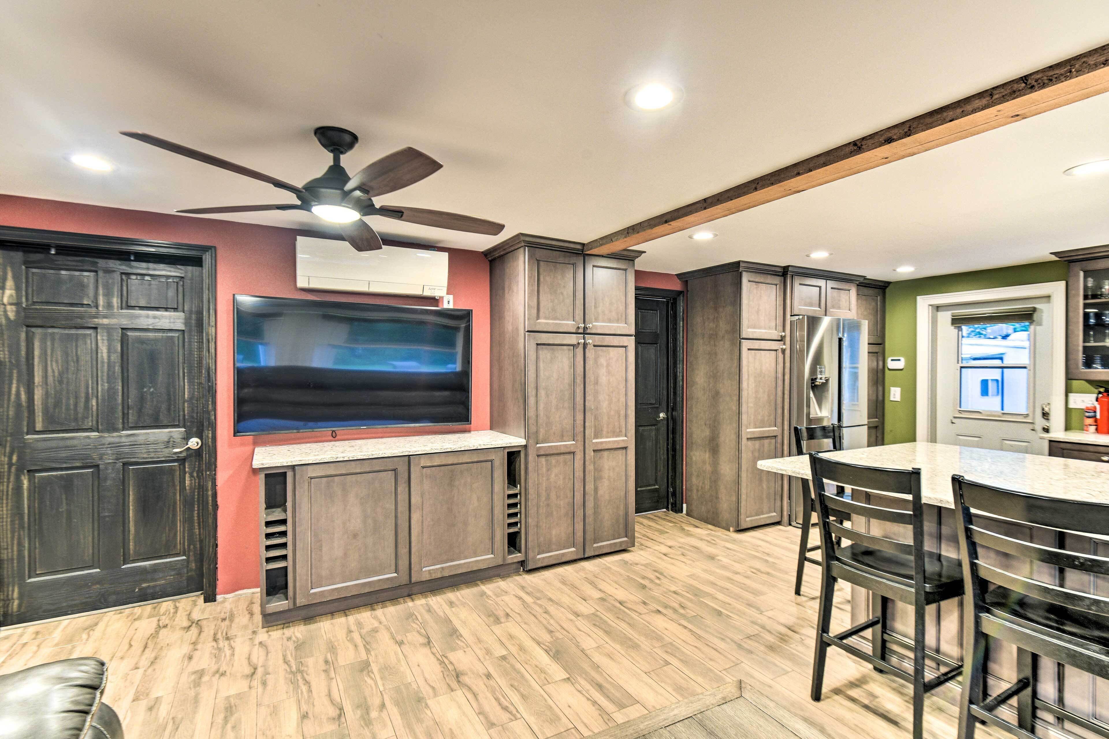 A modern kitchen with dark wood cabinets, a large flat-screen TV, a ceiling fan, and a dining area with bar stools.