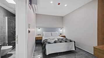 A modern bedroom with a bed, bedside tables, a nightstand, a wall-mounted air conditioner, and a shower area.