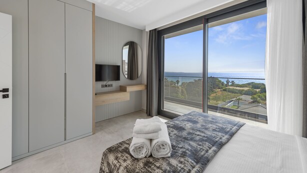 A modern bedroom with a large window, a bed with rolled towels, a TV, and a wardrobe.