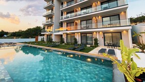 A modern multi-story hotel with a swimming pool, outdoor seating, and balconies.