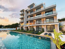 Un hotel moderno de varios pisos con piscina, mobiliario exterior y balcones.