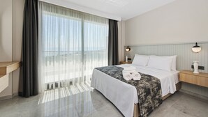 A hotel room with a large bed, a bedside table, a nightstand, and a window with sheer curtains.
