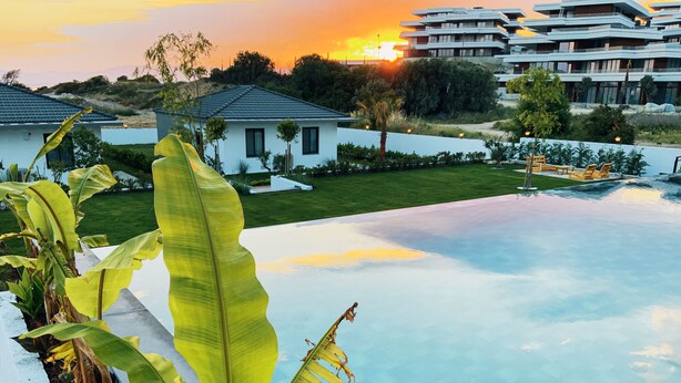 Un hotel moderno con piscina, rodeado de abundante vegetación y vistas al atardecer.