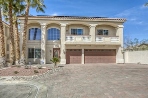 A two-story house with a stucco exterior, a balcony, and a driveway leading to a garage.