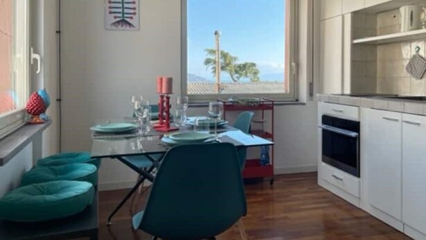 Une cuisine moderne avec des meubles blancs, un coin repas avec des chaises de couleur turquoise et une fenêtre donnant sur des palmiers.