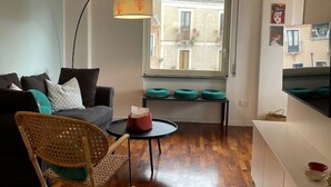 Un salon moderne avec un canapé, un fauteuil à bascule, une petite table et une fenêtre donnant sur des immeubles.