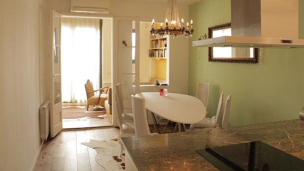 A dining area with a white table and chairs, a chandelier, and a kitchen with a stove and cabinets. - Romantic Design Apartment (Barcelona)