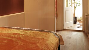 A bedroom with a large bed, a chandelier, a wardrobe, and a door leading to a bright room with a plant. - Romantic Design Apartment (Barcelona)