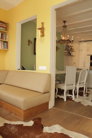A living room with a beige sofa, a dining table with chairs, and a chandelier.