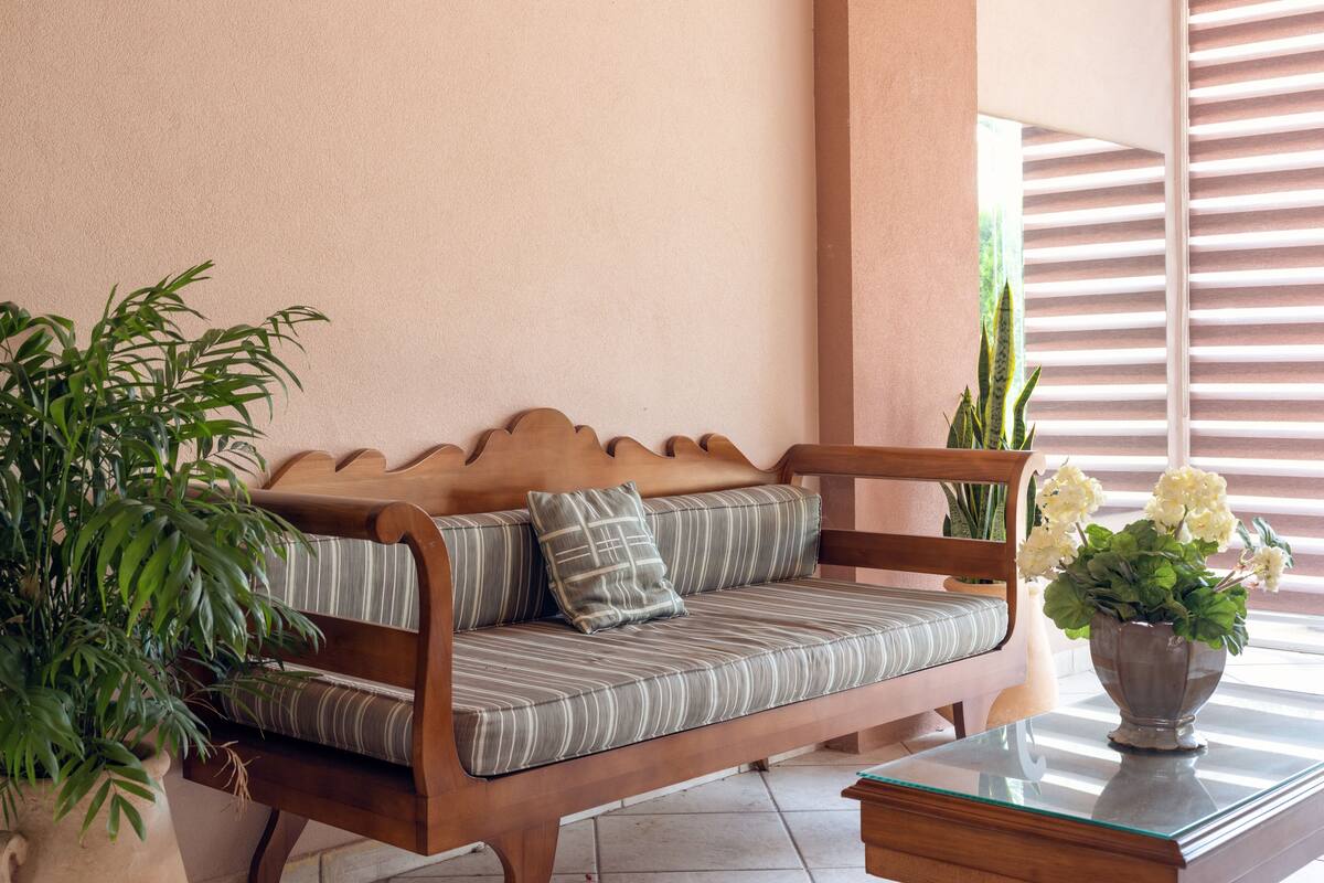 A wooden bench with striped cushions, a potted plant, and a vase with flowers.