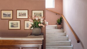 A staircase with a handrail, a wall with framed pictures, and a vase with flowers on a landing. - Villa Maria (Zakynthos)