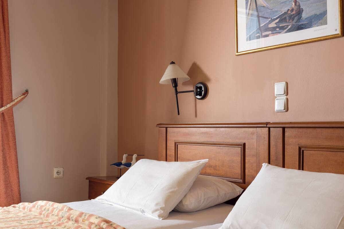 A hotel room with two beds, a wooden headboard, a wall-mounted lamp, and a painting above the headboard.