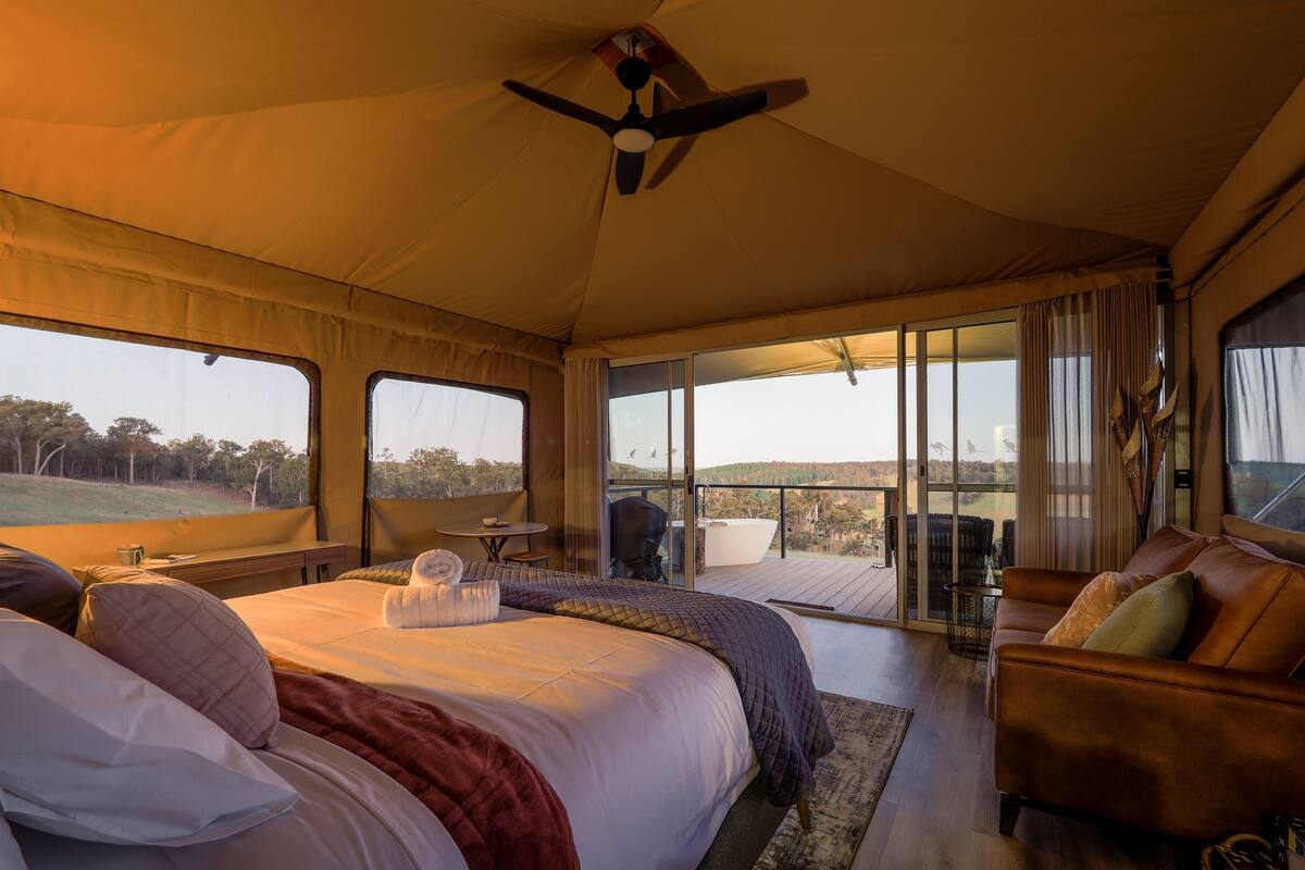 A tented room with a bed, a sofa, and a balcony with a view of the landscape.