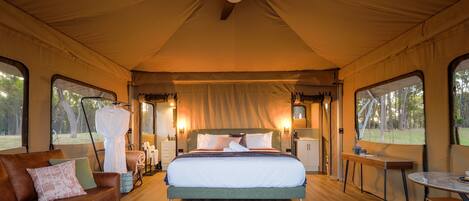 A tented room with a bed, a sofa, a table, and a ceiling fan.