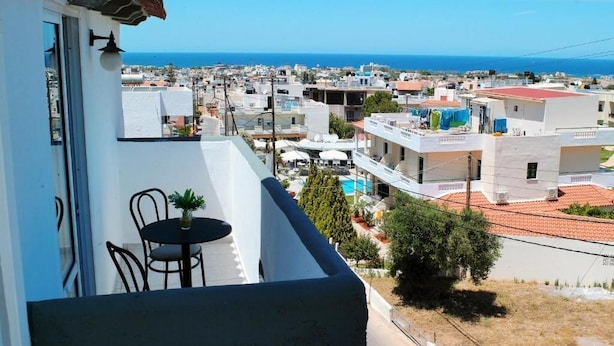 A balcony with a table and chairs overlooking a coastal town with buildings and a clear sky. - Selena View Hotel & Apartments (Hersonissos)